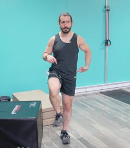 Dr. John with his right leg up at 90 infront of him, pointing at his left hip demonstrating how hes standing upright for the hip mobility exercise